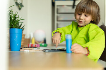 Preschool boy sits at the table and does creative work at home, a child draws with paints, creative...