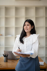 Female office worker holding documents and pen thinking about project and taking notes in office