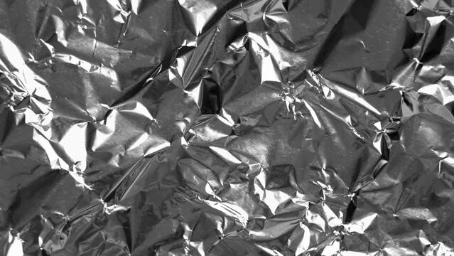 Crumpled glossy sheet of metal foil. Wrinkled silver light abstract pattern. Rotation