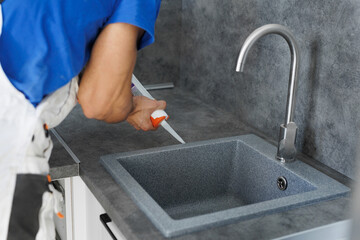 A worker seals up the kitchen sink with a sealant with a construction sealing gun.