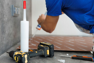 Close-up of gluing a wall panel onto a wall. The man holds a glue gun in his hand. - obrazy, fototapety, plakaty