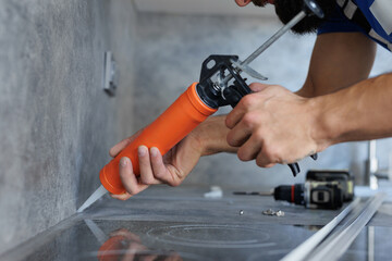 Worker seals up the kitchen countertop with a sealant using a construction sealing gun.