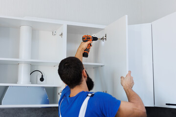 A man in uniform screws the kitchen cabinet doors with an electric screwdriver.