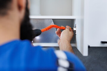 A man screws the kitchen cabinet doors with an electric screwdriver with a flexible nozzle.
