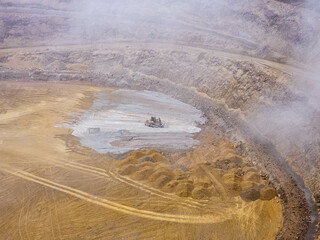 Heavy machinery working at the bottom of an open pit mine on a day with a lot of fog and rain.