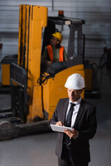 middle aged warehouse manager in business attire and hard hat using tablet while planning logistics - 740019212