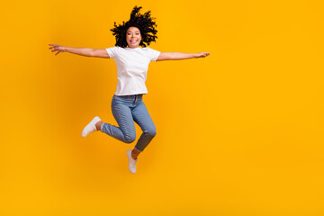 Fototapeta na wymiar Full length photo of positive carefree woman wear white t-shirt jumping arms sides empty space isolated yellow color background
