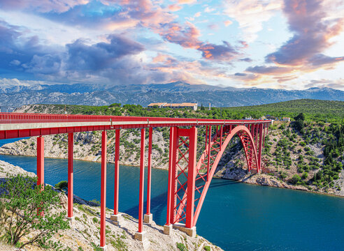 Iron arch bridge with a road against the backdrop of mountains.