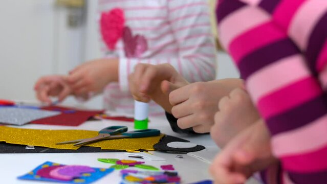 Cute little children cutting color paper with scissors at desk in kindergarten.