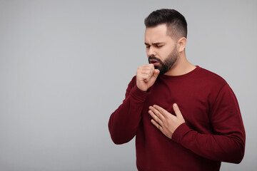 Sick man coughing on gray background, space for text