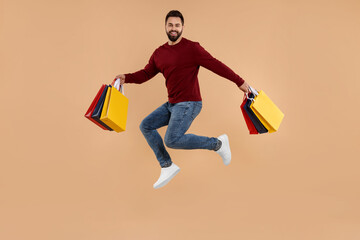 Happy man with many paper shopping bags jumping on beige background
