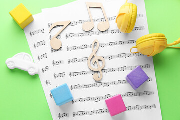 Wooden notes, music sheets, headphones and toys on light green background, flat lay. Baby song...