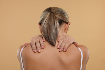 Mature woman suffering from pain in her neck on beige background, back view