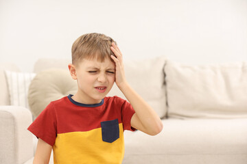 Little boy suffering from headache at home, space for text