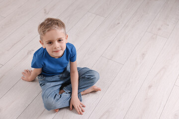 Naklejka premium Cute little boy sitting on warm floor indoors, space for text. Heating system