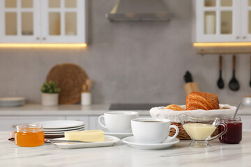 Breakfast served in kitchen. Fresh croissants, coffee, butter, jam, honey and sweetened condensed milk on white table