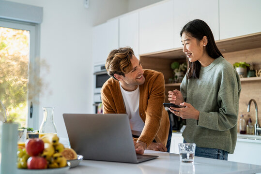 Adult couple shopping online on laptop and smart phone at kitchen counter