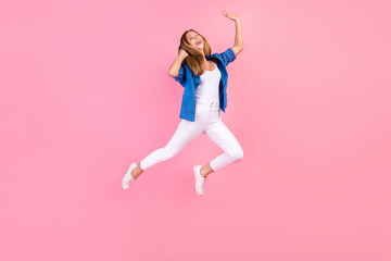 Full length photo of cheerful excited lady dressed blue shirt jumping high enjoying songs earphones singing isolated pink color background