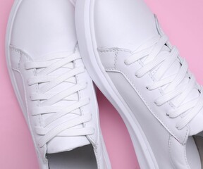 Pair of stylish white sneakers on pink background, top view