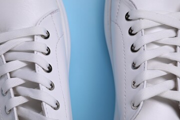 Pair of stylish white sneakers on light blue background, top view