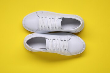 Pair of stylish white sneakers on yellow background, top view