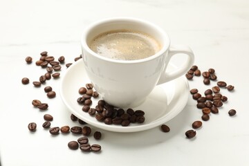 Cup of aromatic coffee and beans on white table, closeup
