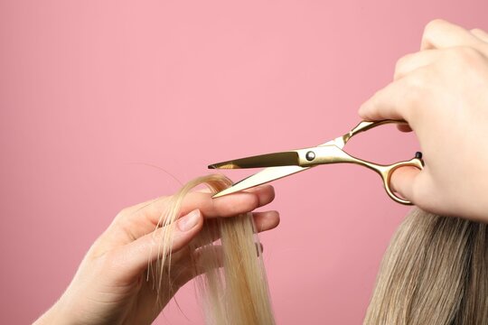 Hairdresser cutting client's hair with scissors on pink background, closeup. Space for text