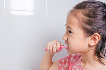 Close up face and mouth of Adorable little Asian girl enjoys her morning routine in relaxed expression for brushing her teeth in clean and bright bathroom for healthy dental care of kid and child.