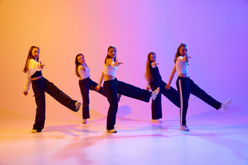 Dynamic image of teen girls training, dancing hip hop, contemporary dance against gradient studio background in neon light. Concept of hobby, youth, childhood, style, fashion, dance school
