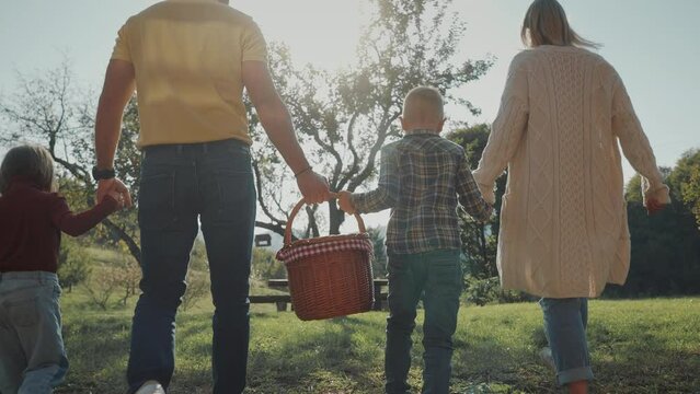 Young familly carrying picnic basket and going for a picnic in the countryside field. Beautiful summer day for family acitivies in the nature.