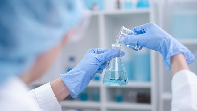Close-up hands holding pouring blue fluid liquid beaker flask test tube glassware sample laboratory for compare in medicine chemical biology medical medicine science experiment technology analysis