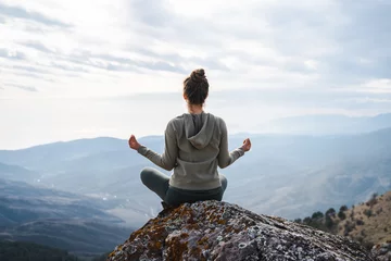 Foto op Plexiglas Woman meditates in yoga asana Padmasana, girl practices yoga and meditates on the mountain, back view of a yogi doing yoga in the mountain © Соня Монштейн