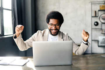 Brazilian businessman exudes joy as he celebrates triumph at laptop, a contemporary office. His...
