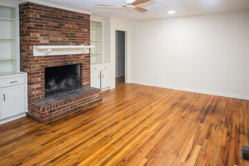 A living room or den with hardwood floors, white walls and a red brick fireplace with mantle in a...