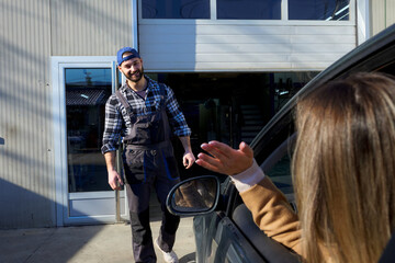 A cheerful mechanic approaches a waving woman customer arriving for service.