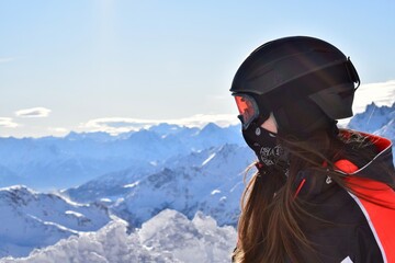 Female skier in winter sports gear with long hair, a black helmet, orange goggles and black face...