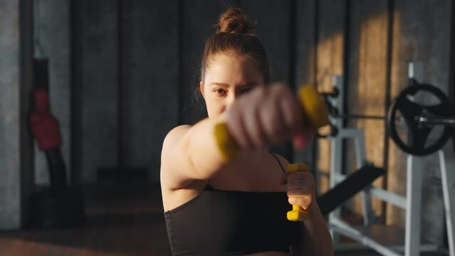 Woman doing exercises with dumbbells. Overweight young girl bodybuilder lifting dumbbell weights in gym, bicep curl exercise training. Sport motivation, athlete training, lose weight concept.