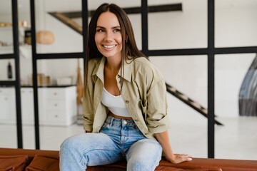 woman sitting on sofa at home relaxed dressed in khaki shirt and jeans