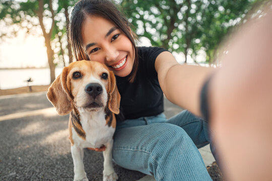Selfie portrait of young asian woman with her beagle dog, in the park in summer.