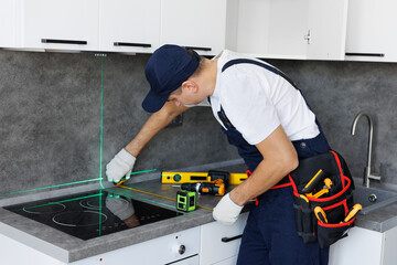 Man in uniform measures the level of the countertop with ruler and laser when assembling furniture.