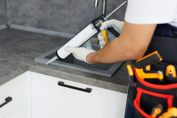 Worker seals up the kitchen sink with a sealant using a construction sealing gun.