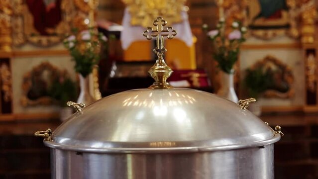 Aluminium church font, large bowl, with golden cross and saint water for the baptism of babies in Orthodox Church temple, Christening ceremony. Concept of rituals, sacraments of the Christian religion