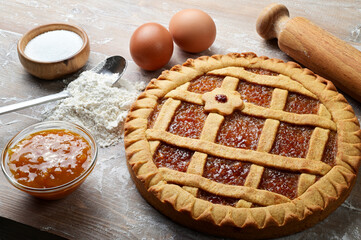 Tart, shortcrust pastry with orange jam, flour, eggs, and sugar on wooden pastry board, closeup. 