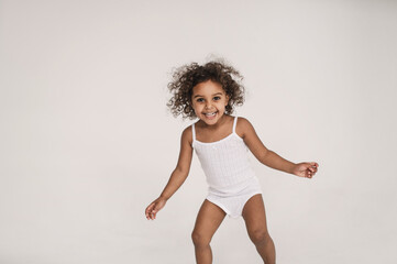 little cute dark-skinned girl 2 years old actively plays and runs on white background. portrait of cheerful, very emotional little black girl screaming. Madness and crazy hyperactivity child