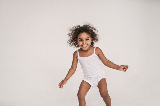 little cute dark-skinned girl 2 years old actively plays and runs on white background. portrait of cheerful, very emotional little black girl screaming. Madness and crazy hyperactivity child