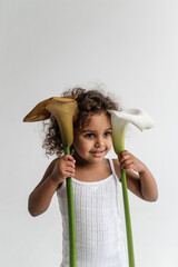 Portrait of little dark-skinned girl 2 years old on gray background holding  calla in her hands....