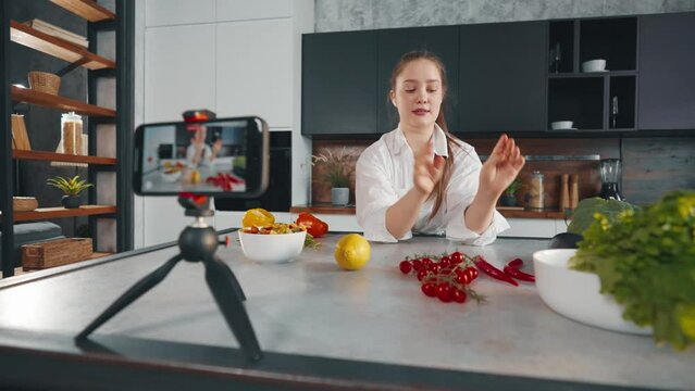 Young woman video lesson about cooking. Positive girl talks recording video lesson, filming cooks tutorial in loft kitchen studio. Concept for online modern cooking courses, recording of training.