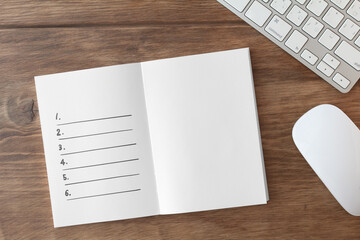 Notebook with lists on brown desk, white keyboard and white mouse