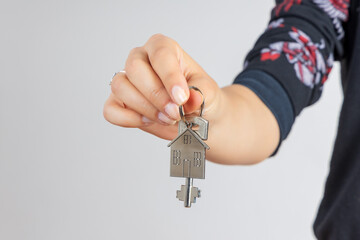 Woman hand giving a new metal key with home shaped keychain, isolated. New home concept - 740061622