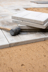 Scene of an ongoing pavement or tile installation. There is a rubber mallet and tiles on top of the partially completed pavement, indicating that the work is in progress.